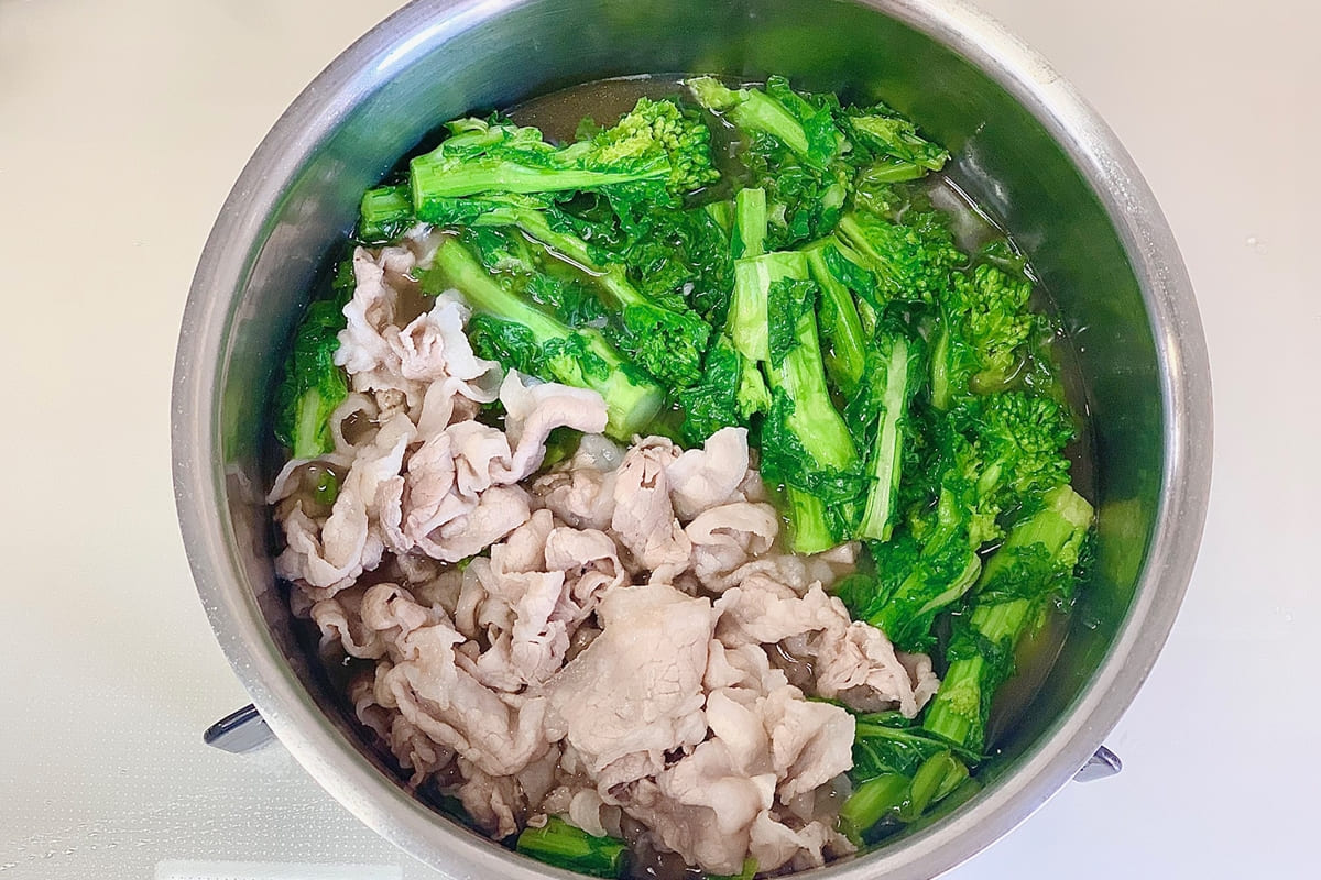 鍋に水、ポン酢、酒、砂糖を入れて火にかけ、豚バラ肉と菜の花を加えて煮る様子